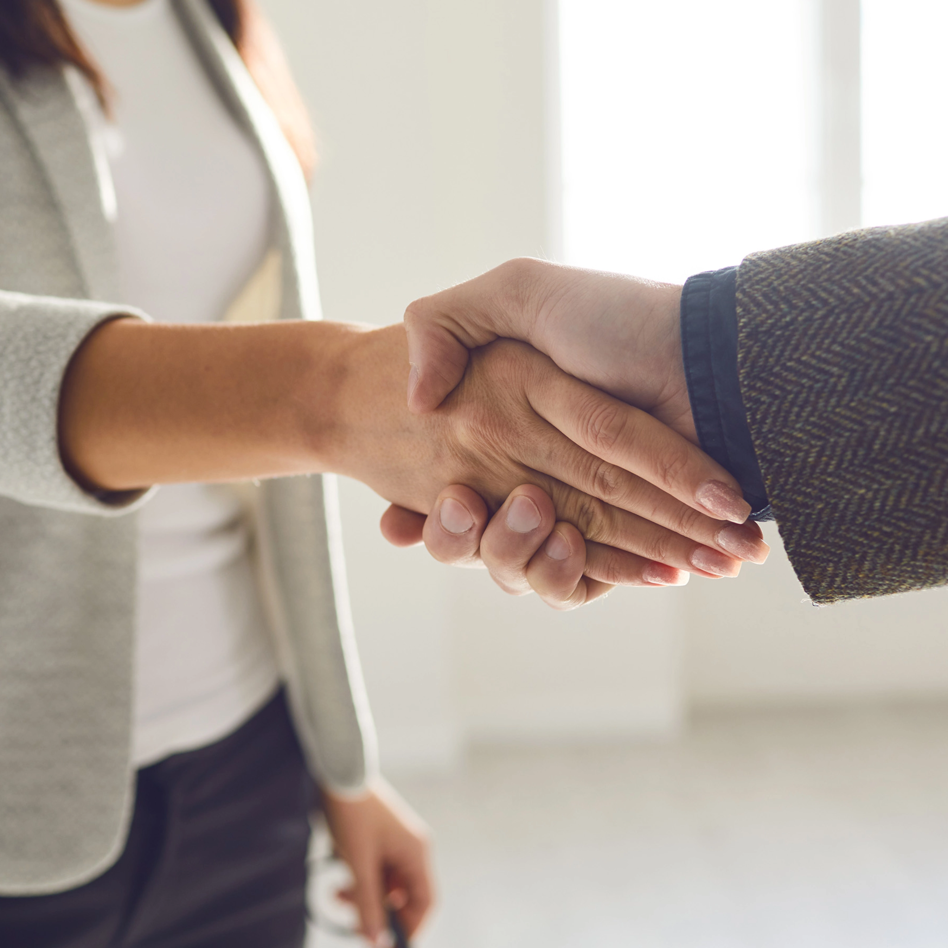Two people in business attire shaking hands in a bright office space.