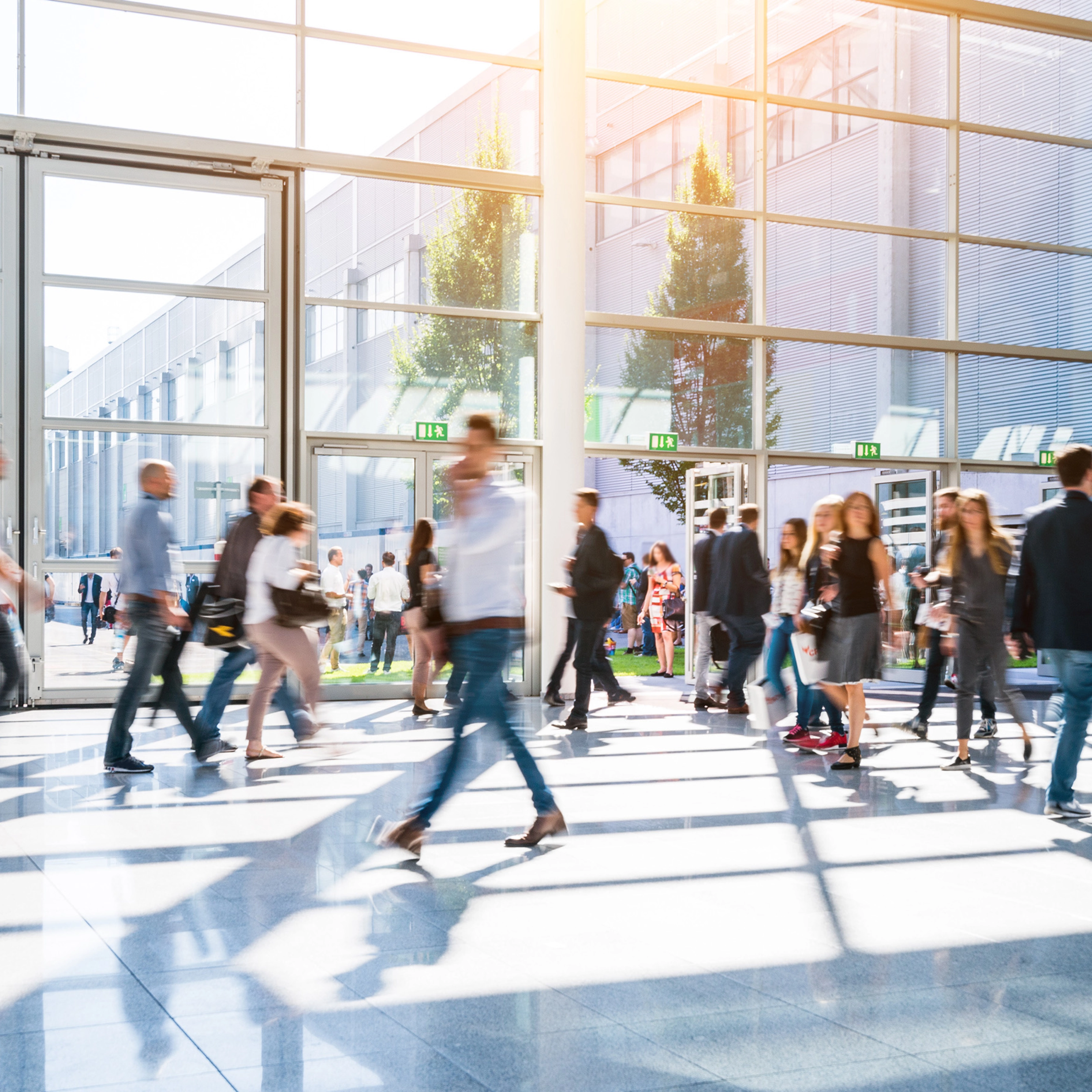 People walk through glass entrances of a modern exhibition hall in daylight.