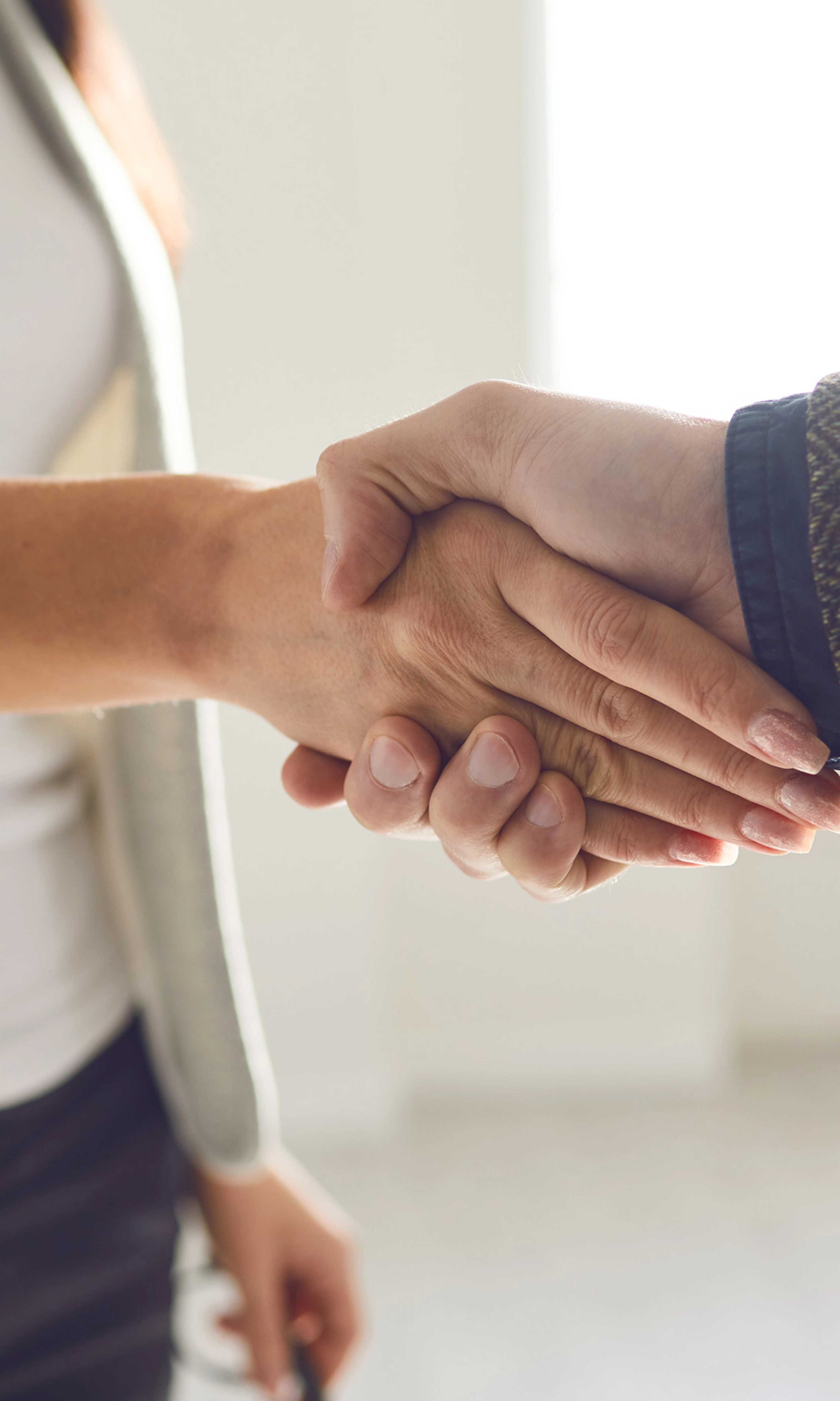 Two people in business attire shaking hands in a bright office space.