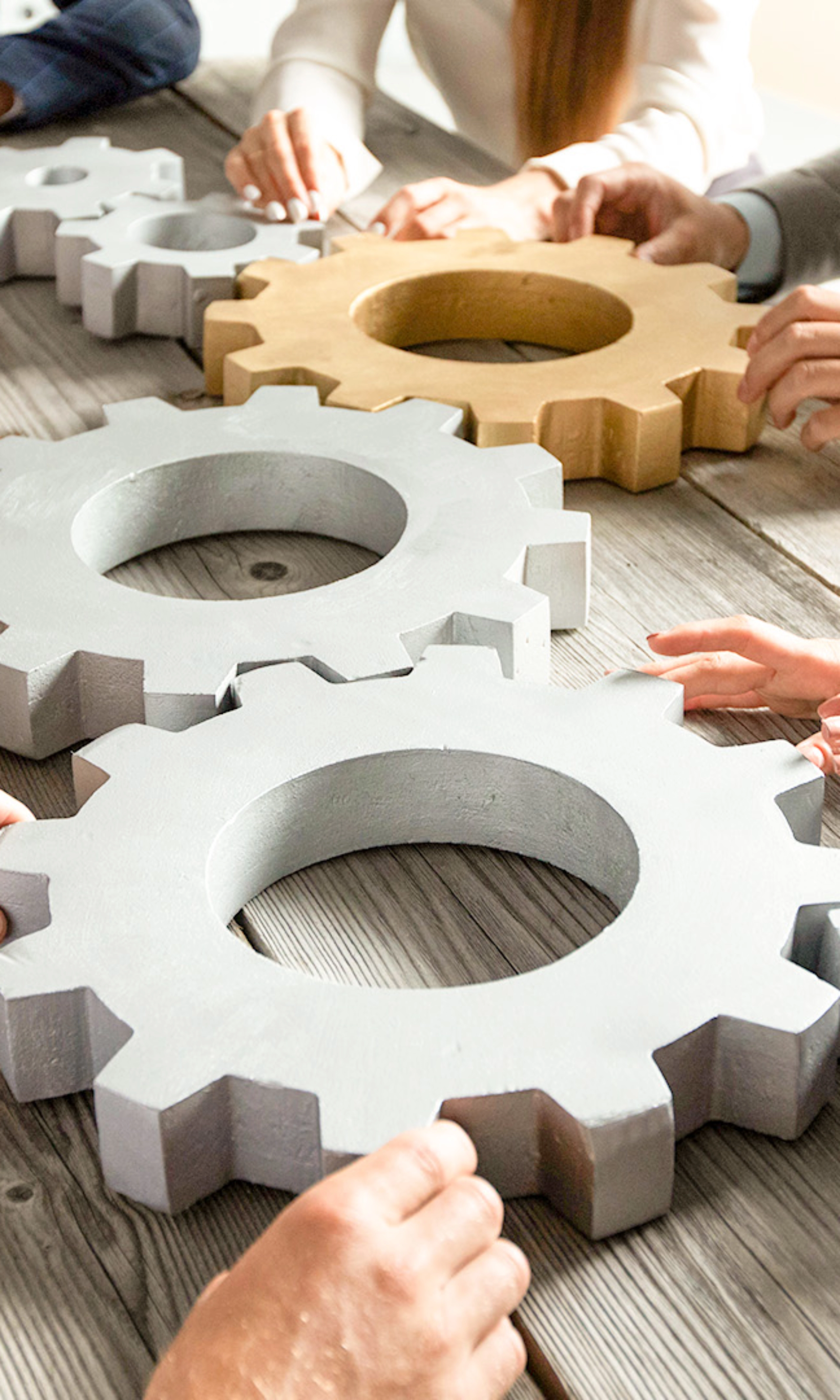 People collaboratively pushing large gears together on a wooden table.