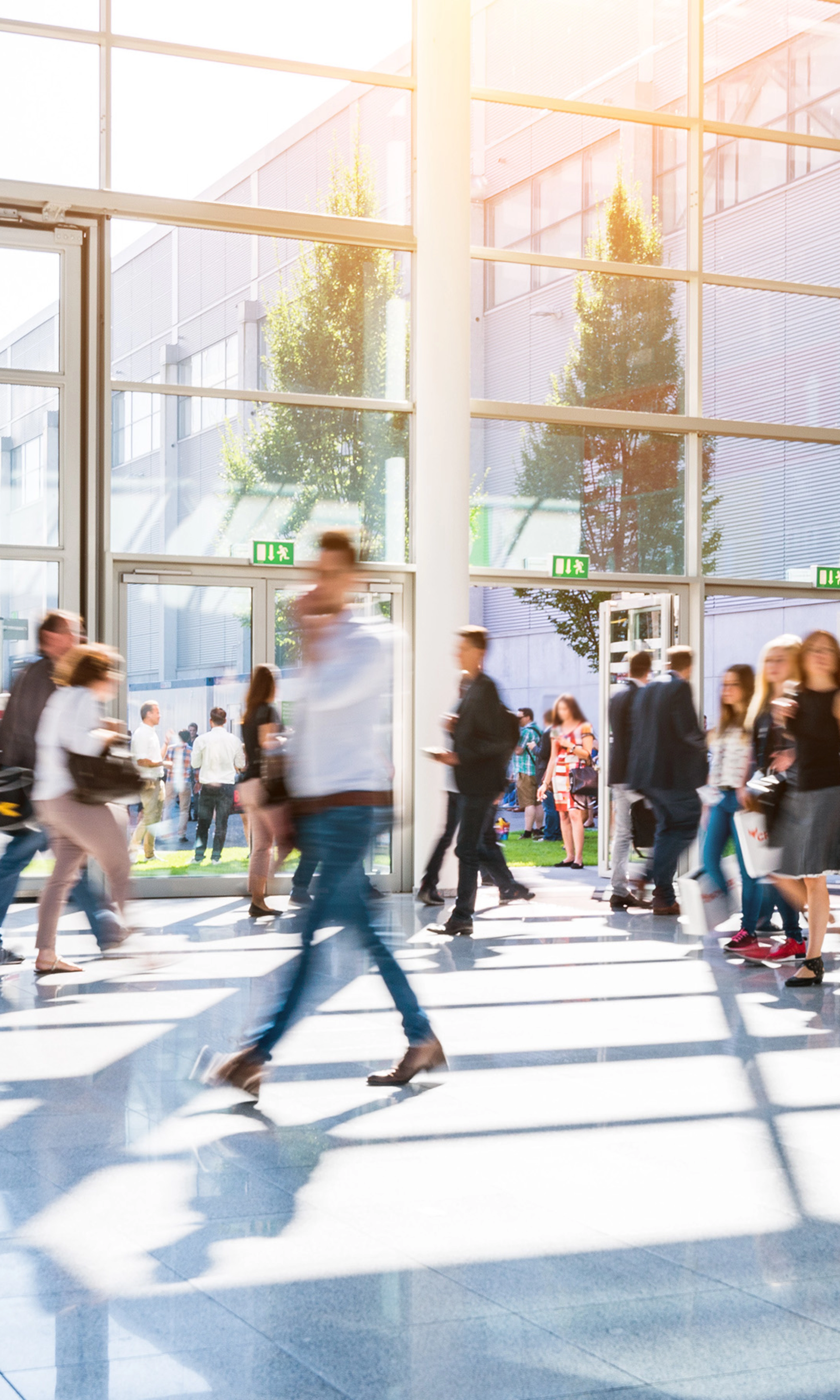 People walk through glass entrances of a modern exhibition hall in daylight.