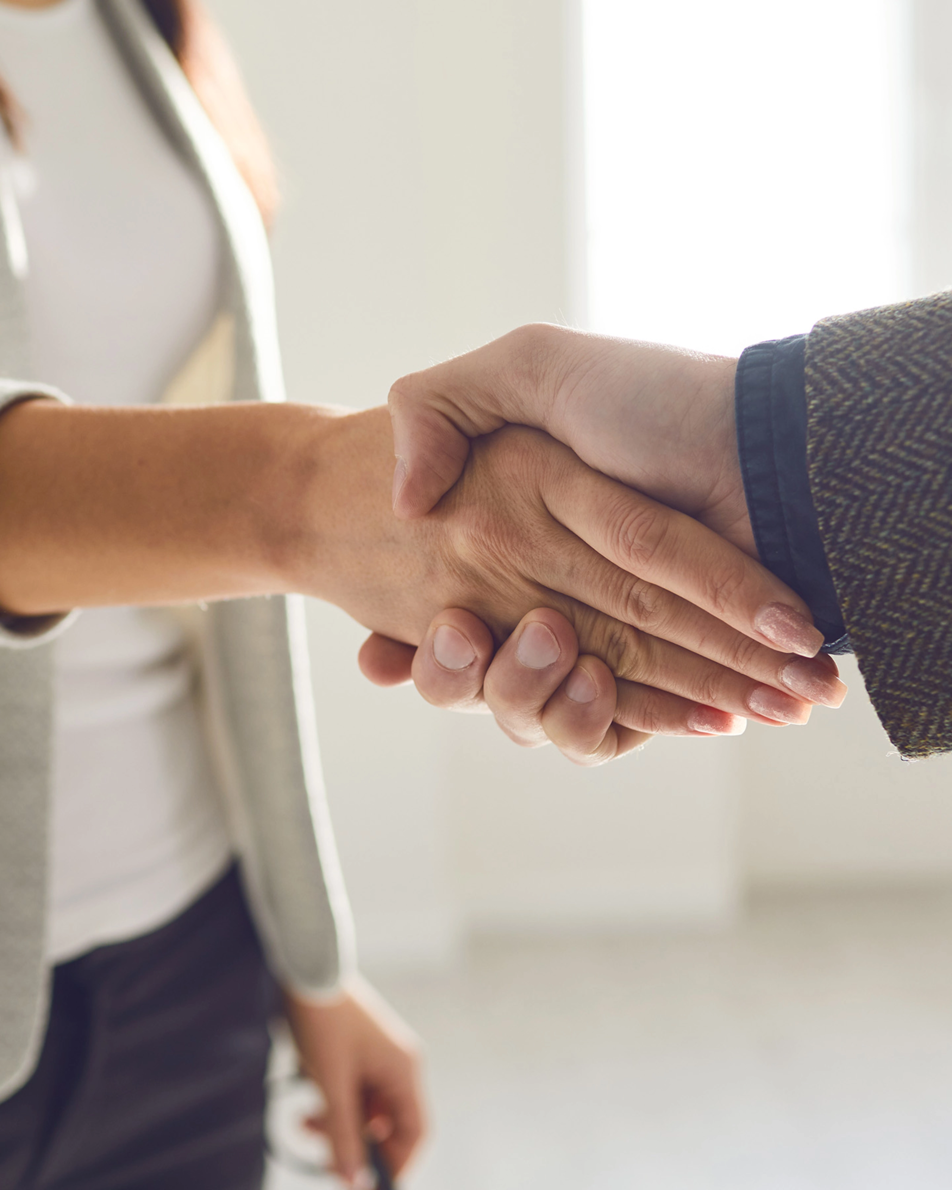 Two people in business attire shaking hands in a bright office space.