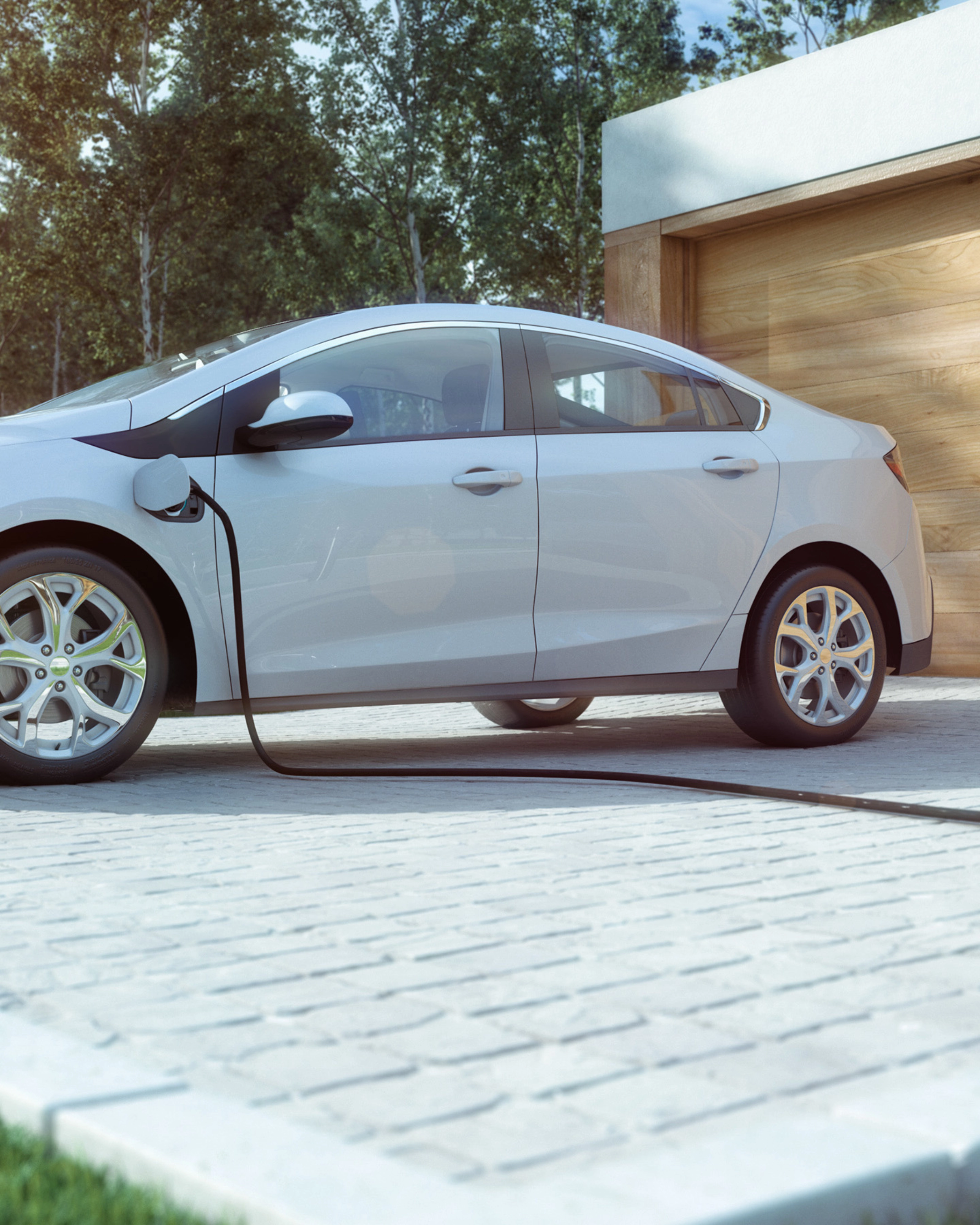 An electric car is charging in front of a modern house with a wooden garage door.