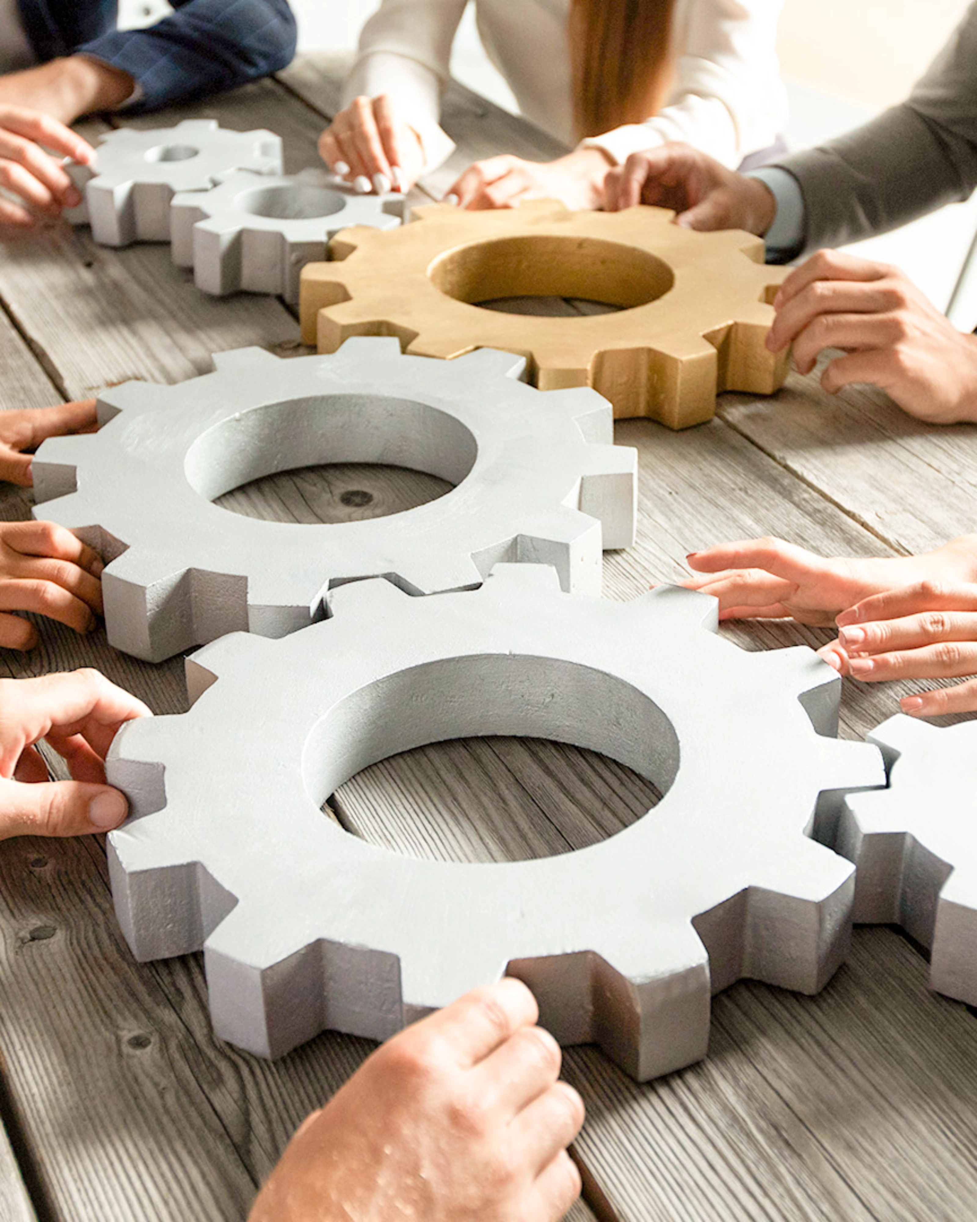 People collaboratively pushing large gears together on a wooden table.