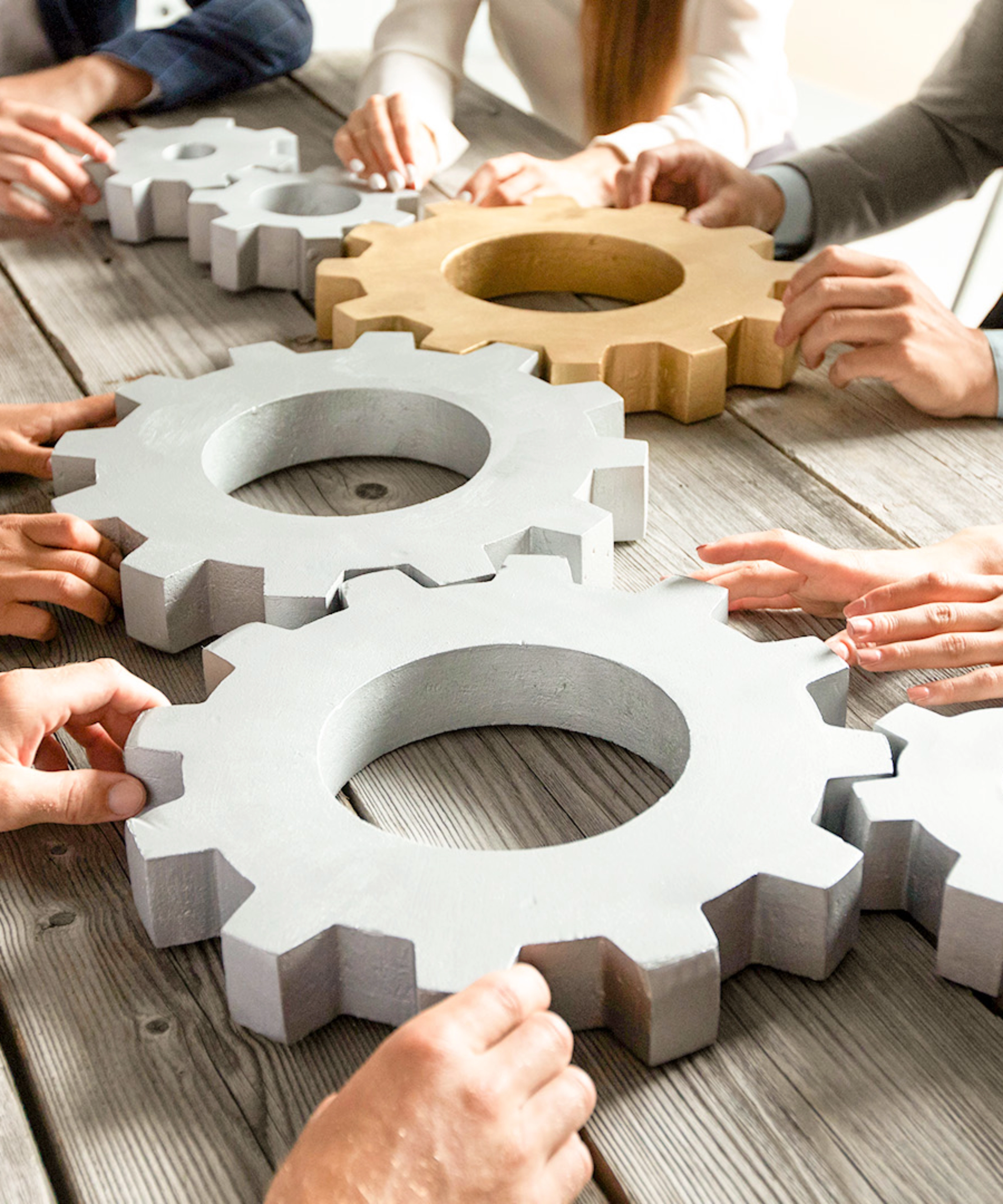 People collaboratively pushing large gears together on a wooden table.