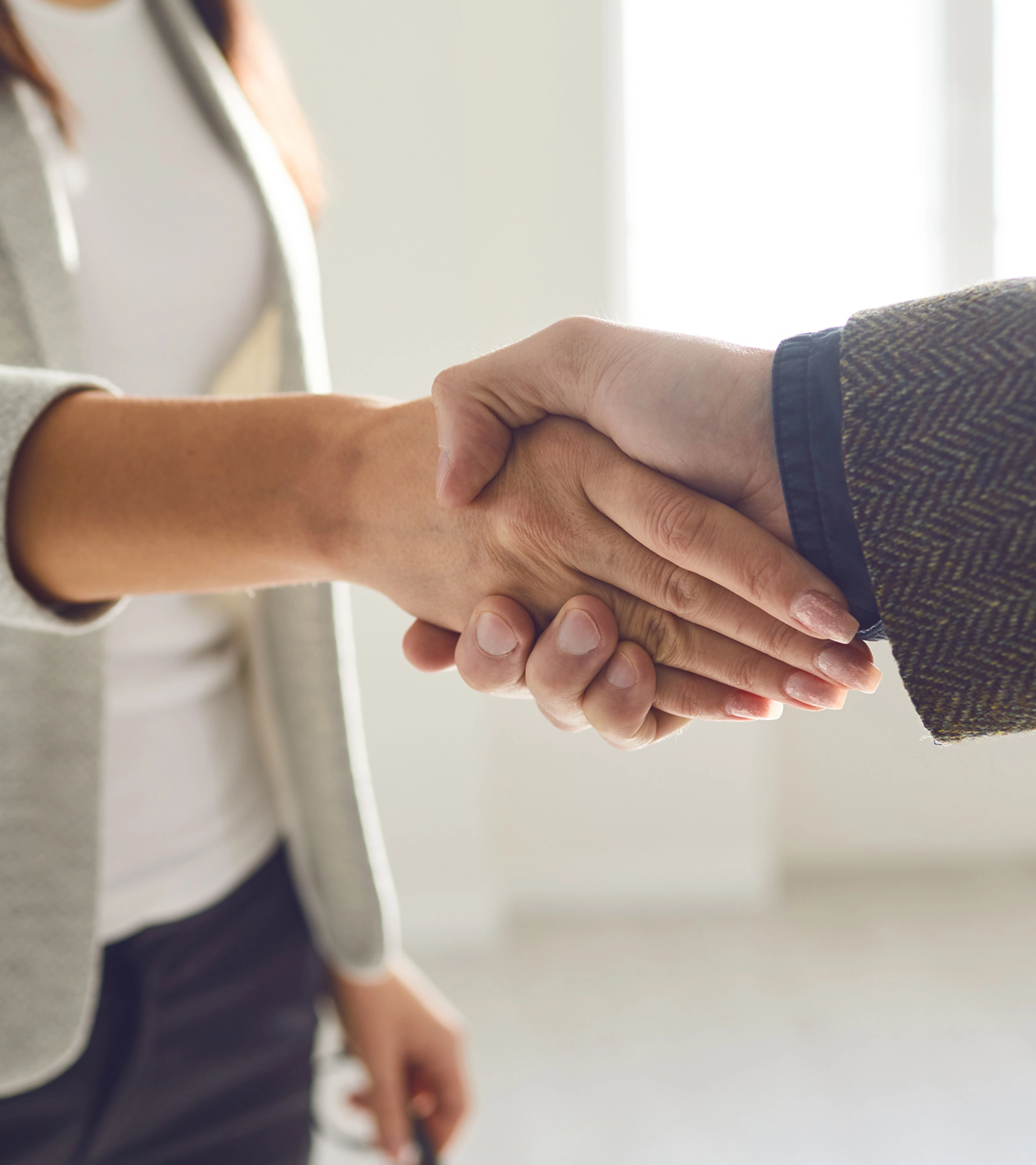 Two people in business attire shaking hands in a bright office space.