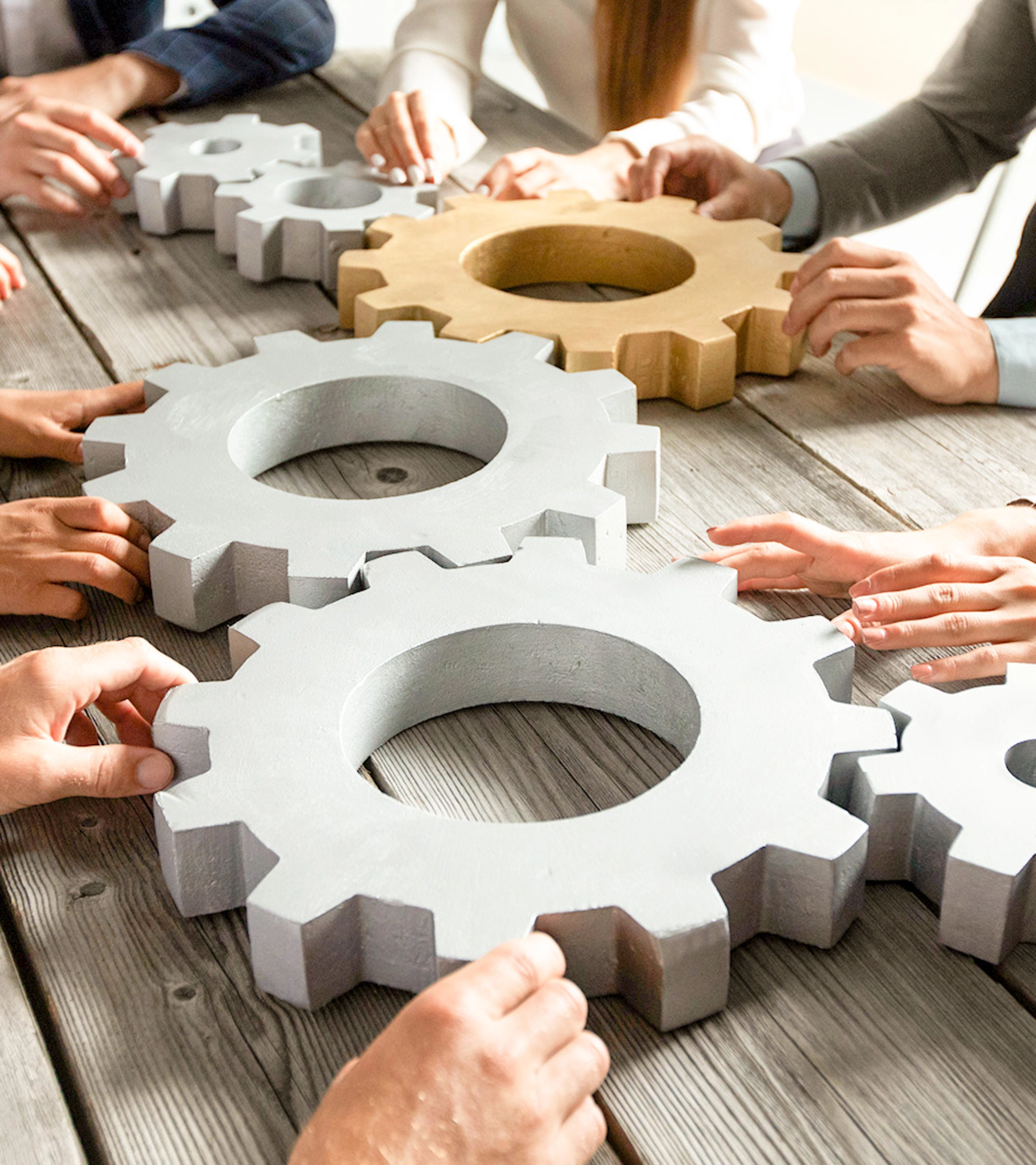 People collaboratively pushing large gears together on a wooden table.
