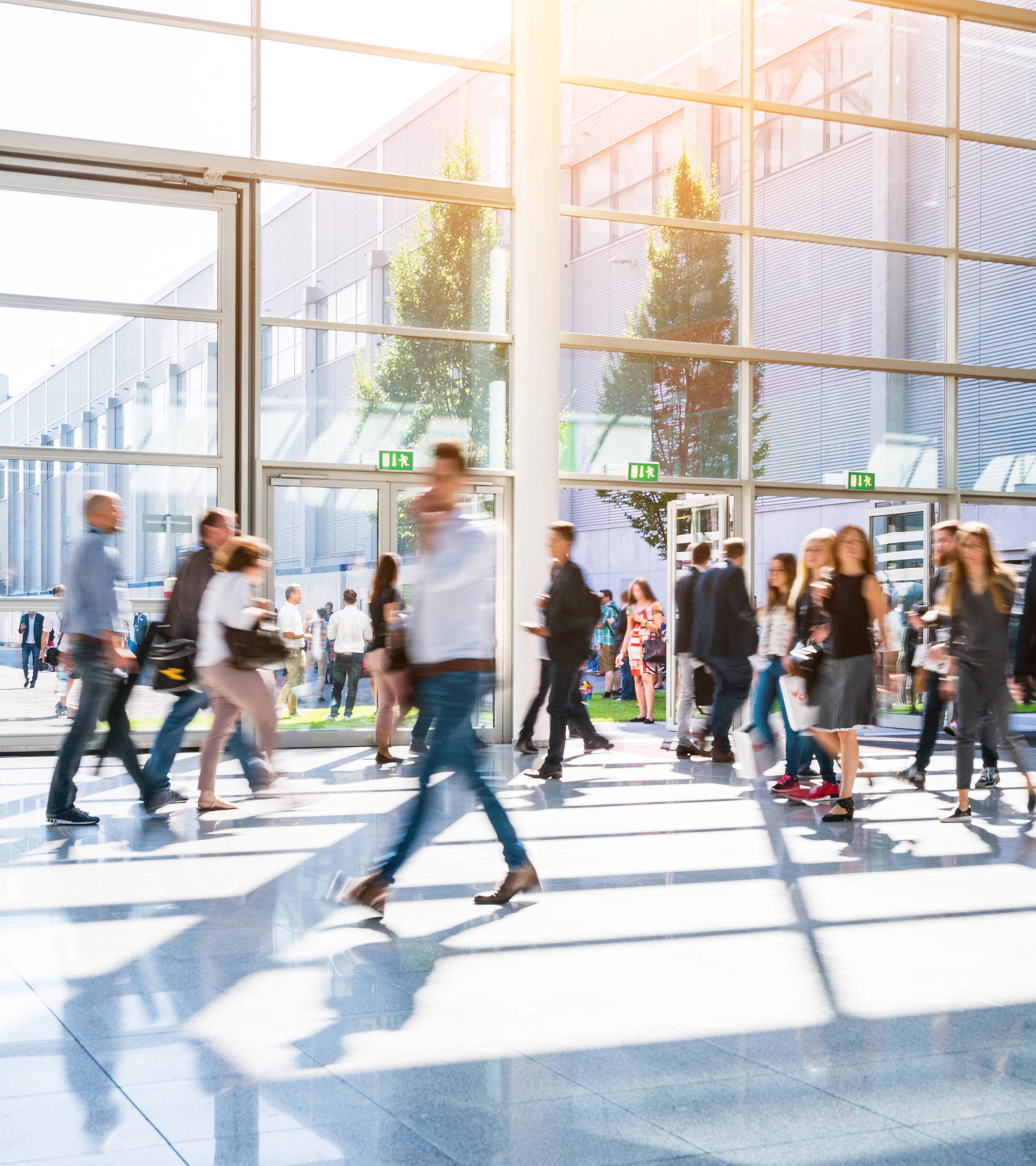 People walk through glass entrances of a modern exhibition hall in daylight.